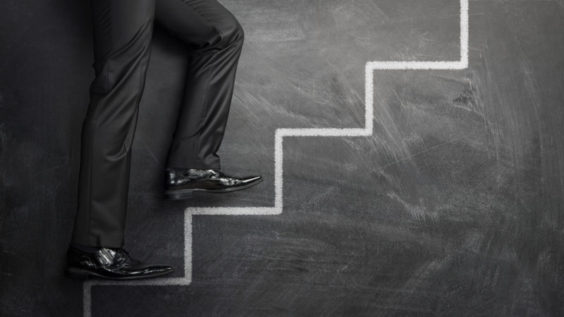 Businessman Climbing The Career Steps Drawn On A Black Chalkboar