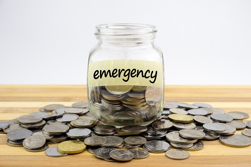 Coins In Glass Container With Emergency Label On Wooden Surface