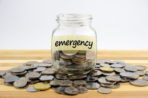 Coins In Glass Container With Emergency Label On Wooden Surface